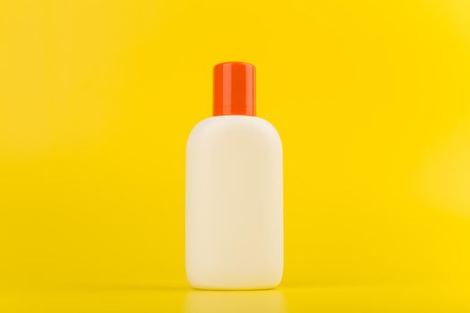 Minimalistic still life with sunscreen cream or lotion with orange cap on yellow background with space for text. Concept of summer skin care and protection