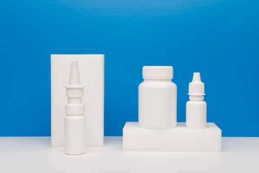 Still life with nose spay, eye drops and pills on white podium against blue background. Concept of healthcare and pharmacy