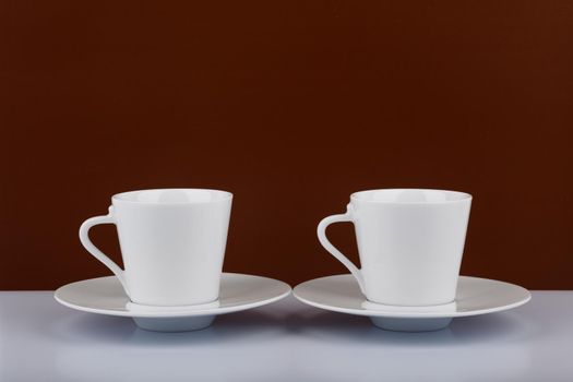 Still life with two coffee cups on white table against brown background with space for text. Concept of hot energy drinks and coffee addiction