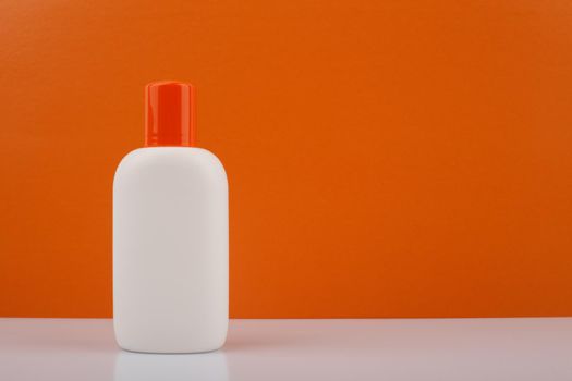 White bottle of sunscreen product with orange cap on white table against orange background with space for text