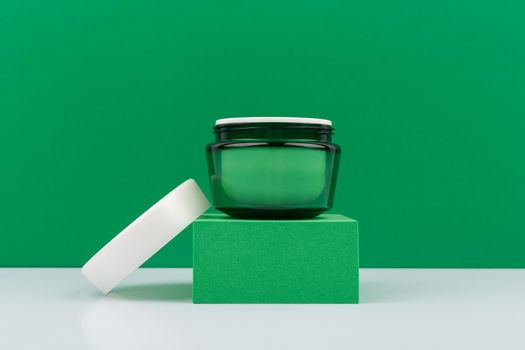 Still life with green cream jar with on green podium against green background on white table. Concept of organic cream or skin care with aloe vera, green tea and natural ingredients