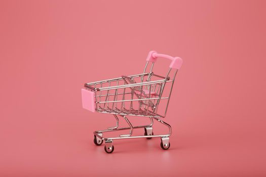 Still life with small decorative shopping cart on pink background. Concept of beauty or online shopping
