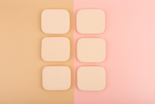 Top view of two rows of square shaped beige make up sponges on pink and beige background. High quality photo