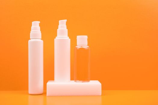 Set of three cosmetic products, face cream, cleaning foam and lotion in a transparent bottle against bright orane background. The concept of daily skin care or anti aging products with fruit extracts