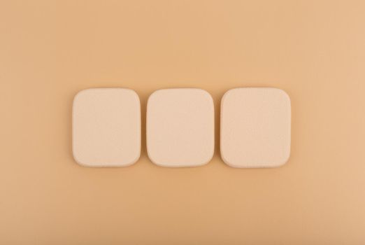 Flat lay with three beige square shape make up sponges on beige background. High quality photo