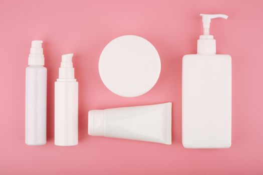 Minimalistic flat lay with set of variety of cosmetic products on pink background. Top view of beauty products for face and body