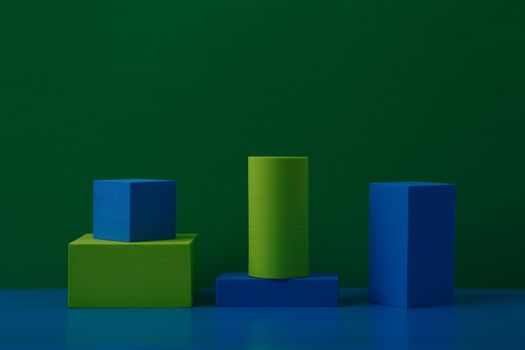 Abstract duotone still life with green and blue geometric figures, square, rectangular and cylinder on blue table with reflection against green background with space for text. High quality photo