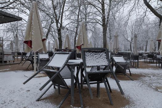 Madrid, Spain - January 07, 2021: Tables and chairs on a terrace, collected, without customers, in the Buen Retiro park in Madrid, in the middle of a snowy day, due to a wave of polar cold.