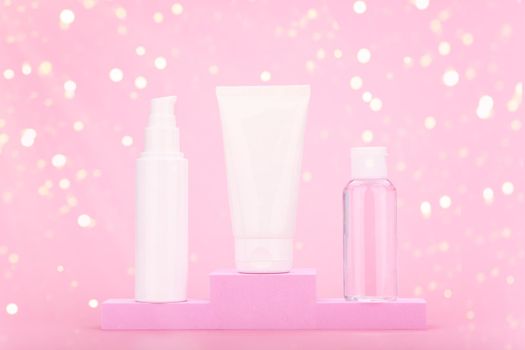 Set of cosmetic products for daily skin care with face cream, cleaning foam and skin lotion on winner pedestal against pink background with yellow bokeh. Concept of cosmetic set gifts and holidays