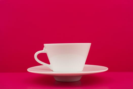 Minimalistic still life with white ceramic coffee cup on a saucer on pink table against pink background with copy space. High quality photo