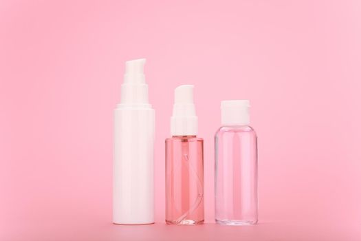 Minimalistic still life with cosmetic set, face cream or gel, cleaning foam and lotion in transparent bottle with white caps against bright pink background. 