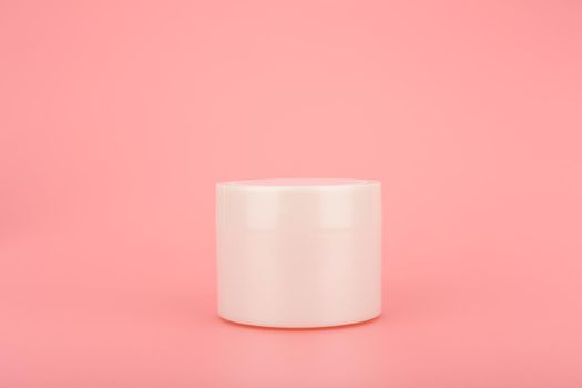 Close up of white unbranded cream jar on pink background with space for text . Minimalistic concept of beauty and skin care 
