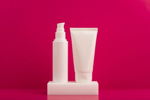 Still life with two white unbranded cream tubes on white podium against pink background. Concept of skincare and beauty products or face and body cream