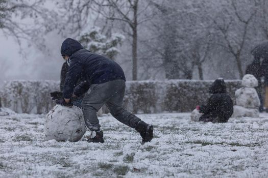 Madrid, Spain - January 07, 2021: Children playing with snow and making snowmen, in the Buen Retiro park in Madrid, in the middle of a snowy day, due to a wave of polar cold.