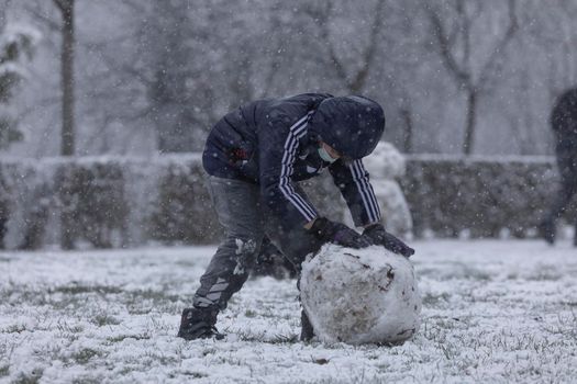 Madrid, Spain - January 07, 2021: Children playing with snow and making snowmen, in the Buen Retiro park in Madrid, in the middle of a snowy day, due to a wave of polar cold.