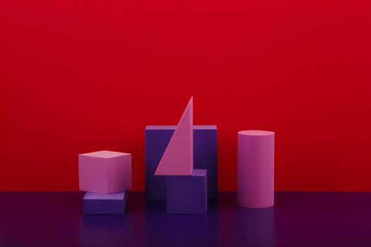 Still life with geometric composition with purple figures on purple shiny table against red background with copy space. High quality photo