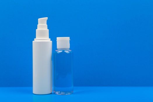 Simple still life with face cream and lotion on blue table against blue background. Concept of hygiene and skincare or special needs treatment
