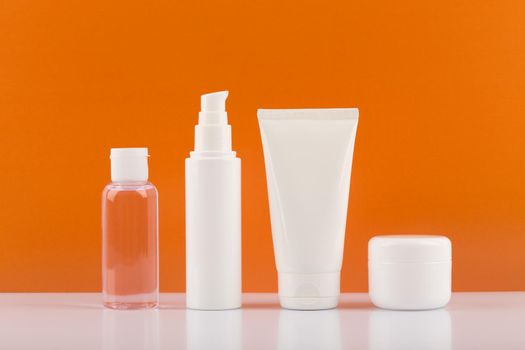 Minimalistic still life with a set of skincare cosmetics on white glossy table against orange background. Concept of skincare and wellbeing or beauty products for daily routine