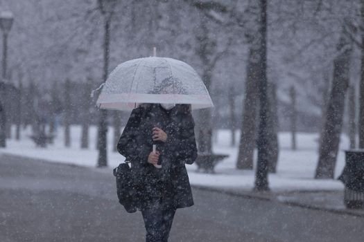 Madrid, Spain - January 07, 2021: A young girl walks fast in the middle of the blizzard, through the Buen Retiro park in Madrid, in the middle of a snowy day, due to a wave of polar cold.