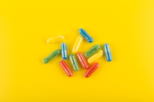 Minimalistic flat lay with spilled green, red, blue and yellow pills on bright yellow background. High quality photo