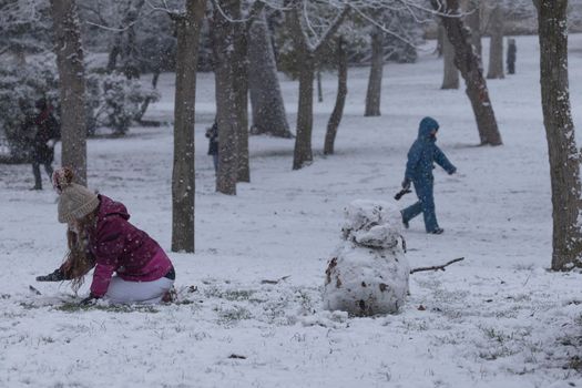 Madrid, Spain - January 07, 2021: Children playing with snow and making snowmen, in the Buen Retiro park in Madrid, in the middle of a snowy day, due to a wave of polar cold.