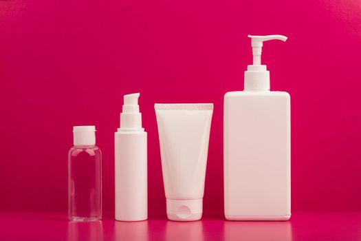 Body cream, face cream, cleaning foam and lotion in a row on pink background