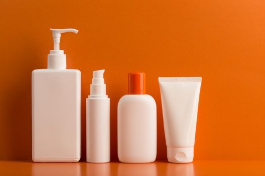 Colorful orange still life with set of cosmetic products for skin and body care against orange background. Concept of sunblock or sunscreen products, creams, balms amd lotions