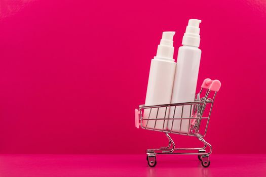 Two white unbranded creams in shopping cart against pink background. Concept of beauty and skincare or online shopping