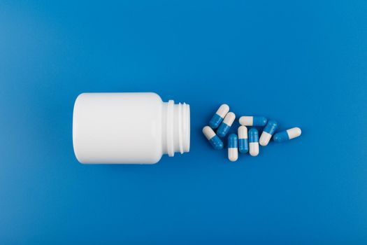 White unbranded medication bottle with spilled duotone oval pills on blue background. High quality photo