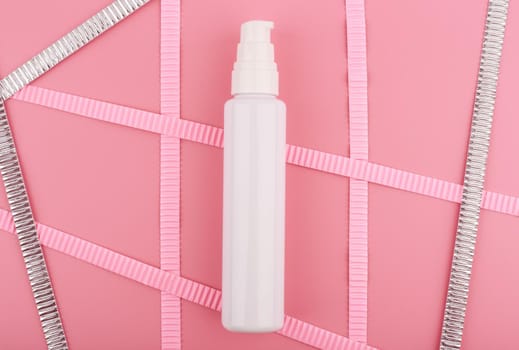 White cream tube on bright pink background with pink and silver stripes. Concept of beauty and skin care