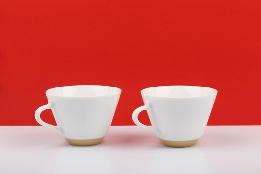 Still life white ceramic shiny coffee cups on white table against red background with space for text. Concept of hot drinks