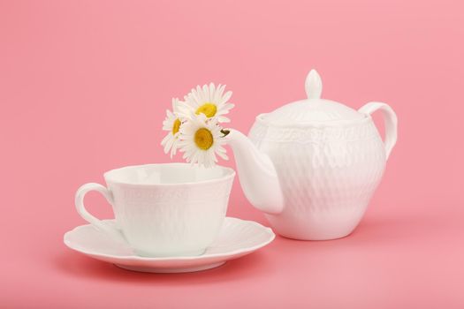 Still life with white porcelain tea pot with camomile flowers and tea cup on pink background. Concept of herbal tea and healthy lifestyle. High quality photo