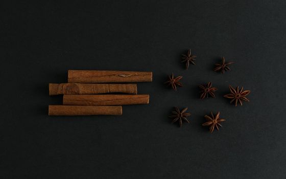 Four big cinnamon sticks and anise stars flatlay on black background