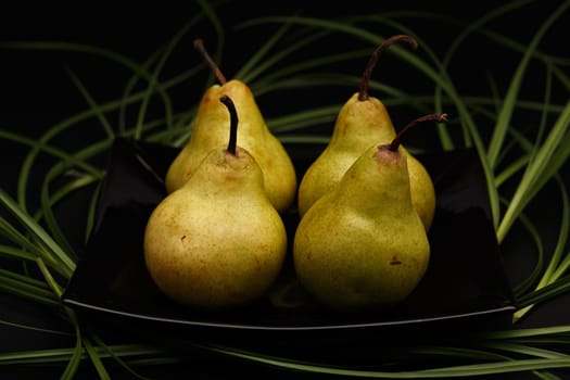 Four pears on black glossy plate decorated with green grass