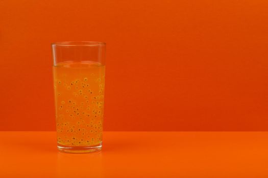 Creative minimalistic still life with fresh fruit juice in transparent glass on orange background with space for text. The concept of healthy lifestyle, wellbeing or importance of vitamins