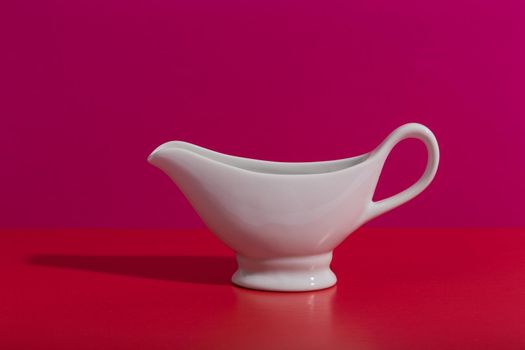Still life with white ceramic sauce boat on creative red and pink background with space for text. High quality photo