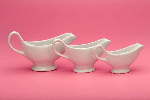 Simple creative still life with white ceramic sauce boats on pink background