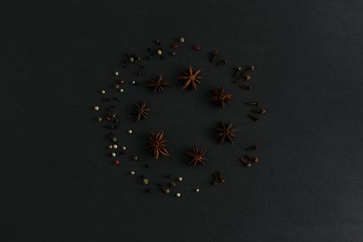 Round composition of anise stars, colorful pepper and clove sticks on black background