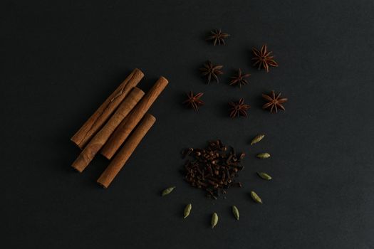 A composition of cinnamon sticks, anise stars, clove and cardamon seed on black background in dark key