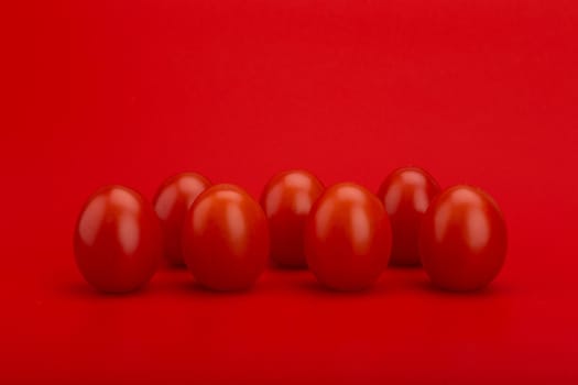 Still life with red cherry tomatoes in a row on red background with space for text. Concept of vegan food or healthy lifestyle