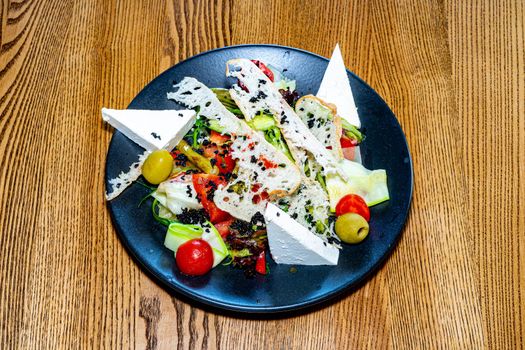 Salad on a plate. Salad with cheese, bread, ofochas and fruits on a black plate.