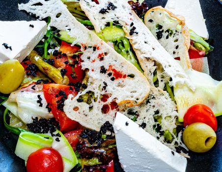 Salad on a plate. Salad with cheese, bread, ofochas and fruits on a black plate.