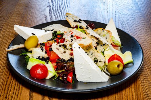 Salad on a plate. Salad with cheese, bread, ofochas and fruits on a black plate.