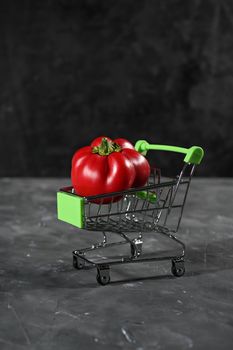 pepper in the tiny supermarket cart on black. The concept of healthy eating