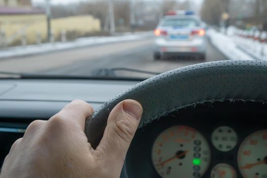 the driver's hand on the steering wheel of a car that is driving on the road behind a police car