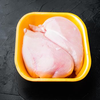 Raw chicken breast fillets in tray, on black background