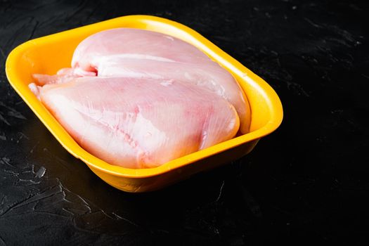 Raw chicken breast fillets in tray, on black background with copy space for text