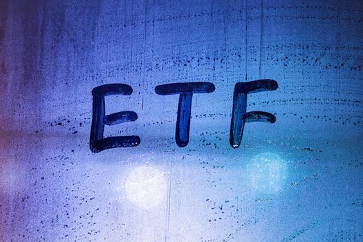 abbreviation word etf - exchange traded funds - handwritten on foggy glass window at night with neon blue back street lights