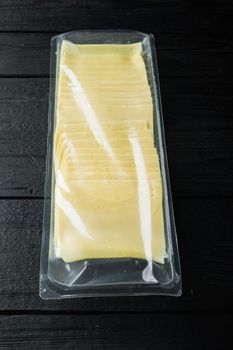 Slices of yellow cheese, sealed pack, on black wooden table