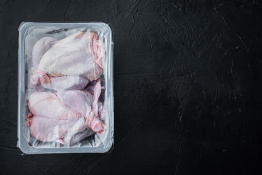 Raw chicken set in plastic vacuum tray, on black background, top view with copy space for text